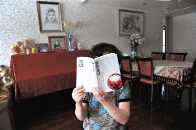 去年7月，北京一名失独母亲，举着她写给女儿的书《你曾来过》，背后是女儿的钢琴和画像。新京报记者 尹亚飞 摄